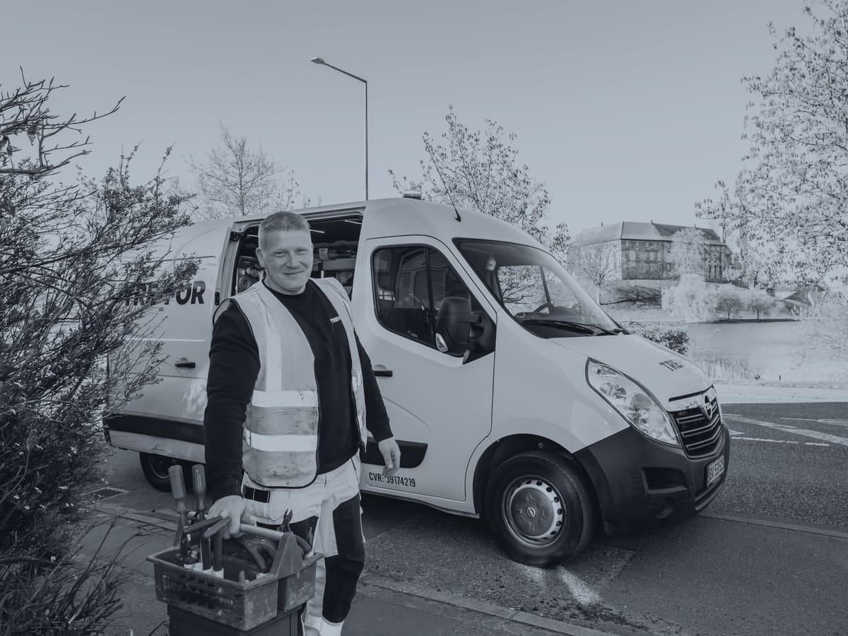 Tradesperson in a reflective vest standing at the back of a work van holding tools